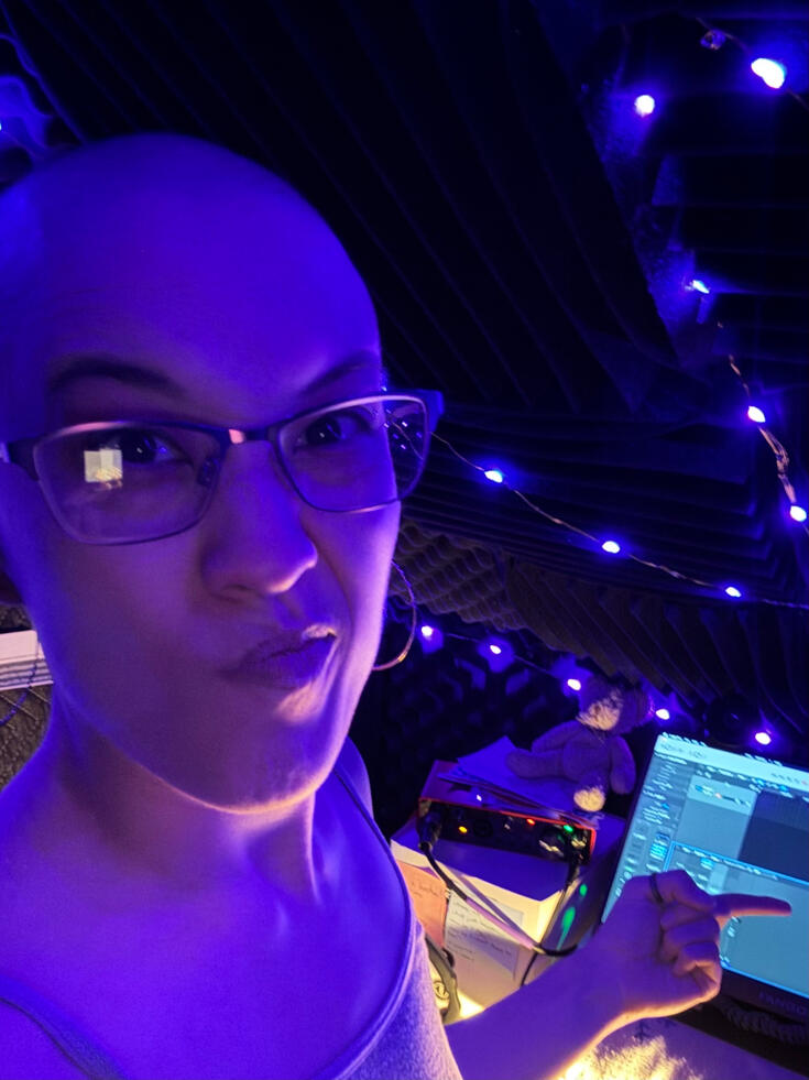 A picture of D Casellian being very serious in her booth A picture of D Casellian being very serious in her vocal booth, which is lit by purple string lights.